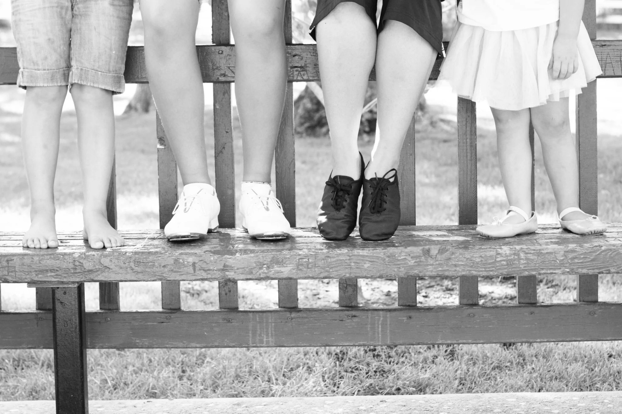 Four dancers wearing different styles of dance shoes in black and white
